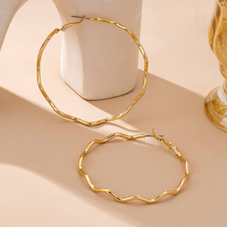 Gold hoop earrings on a beige surface with a soft focus background