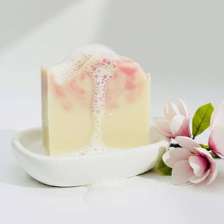 Bar of soap with lather on a white dish, accompanied by pink flowers on a light background