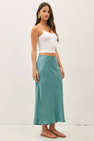 Woman wearing a white top and teal skirt on a plain background