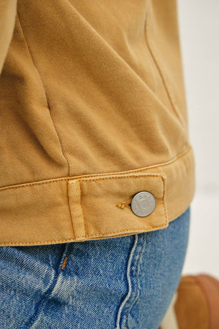 Close-up of a mustard yellow corduroy jacket with a silver snap button detail, worn over blue denim jeans.