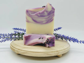 Two swirled purple and white soap bars on a wooden stand with lavender flowers.