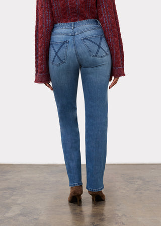 A model viewed from the back wearing medium-wash blue jeans with a distinctive crossed-stitch pattern on the back pockets, styled with a textured red sweater and brown boots against a white studio background.