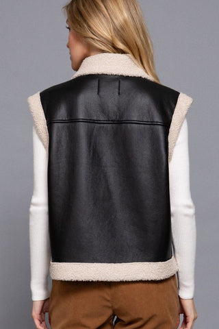 Black leather vest with beige interior and trim worn by a person on a gray background
