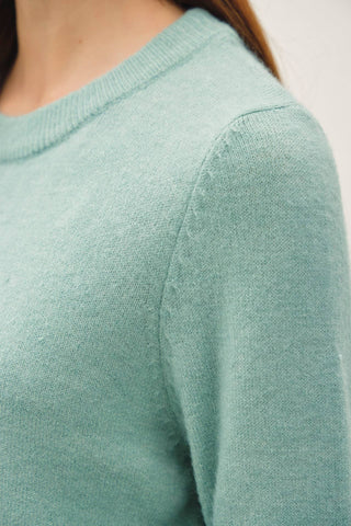 Close-up of a person wearing a soft mint green knit sweater, showing the crew neckline and shoulder area against a plain light background.