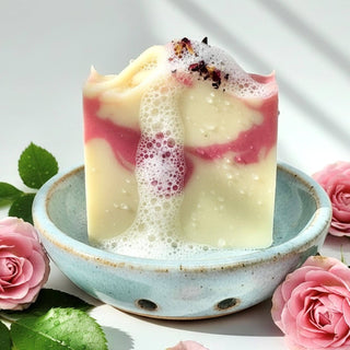 Decorative candle with pink and white swirls in a blue ceramic dish, surrounded by pink roses and green leaves.