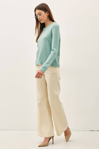 A woman modeling a light mint green long-sleeve knit sweater, paired with cream wide-leg trousers and beige pointed-toe heels, standing against a plain off-white studio background.