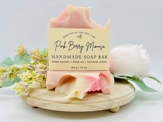 Handmade soap bar with a label on a wooden stand, surrounded by flowers.