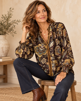 Woman wearing a floral blouse and dark jeans sitting on a stool