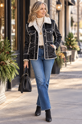 Woman wearing a black coat, a white turtleneck and jeans walking along a sidewalk