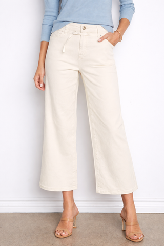 Person wearing light-colored wide-leg pants and a blue top against a white wall.