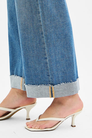 Close-up of blue jeans with a cuffed hem and white sandals on a white background
