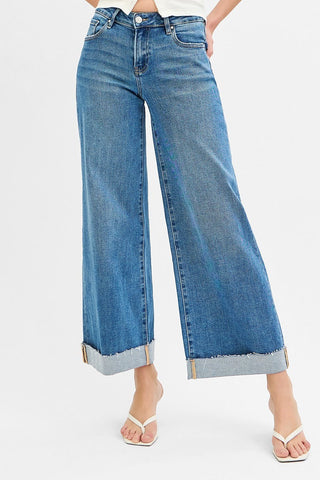 A person wearing blue wide-leg cropped jeans with rolled cuffs, paired with white flip-flop sandals, shown against a plain light gray studio background.