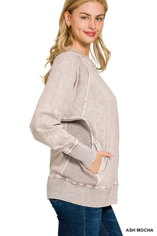A woman modeling a light ash mocha long-sleeve sweatshirt with a raw-edge washed finish and side pockets, paired with blue jeans against a white background.