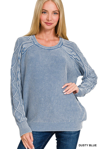 Woman wearing a dusty blue sweater with cable knit details on a white background
