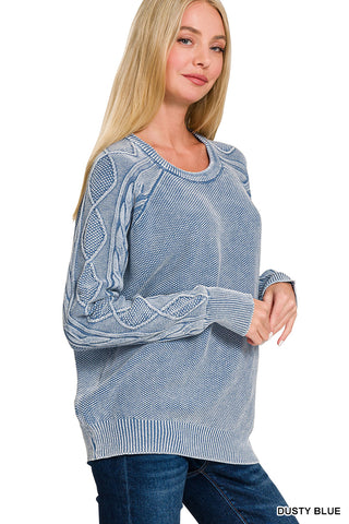 Woman wearing a dusty blue sweater with cable knit sleeves on a white background