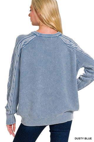 Blue sweater with cable knit sleeves worn by a person on a white background