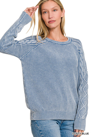 Woman wearing a dusty blue sweater with cable knit details on a white background