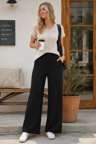 Woman in black pants and white shirt holding a coffee cup outdoors.