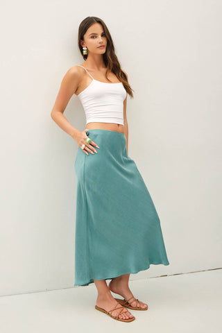 Woman wearing a white top and teal skirt against a white background