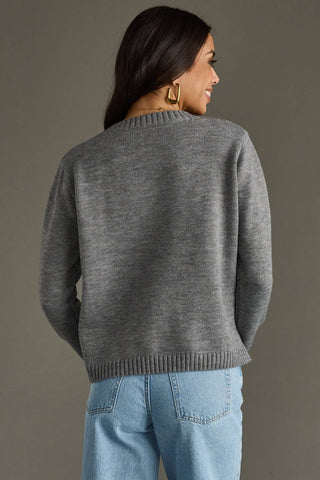 Woman wearing a gray sweater and blue jeans against a neutral background