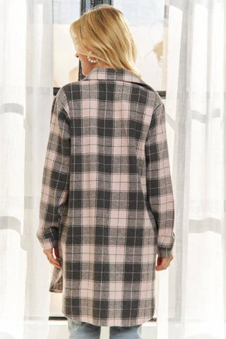 A woman viewed from behind wearing a long-sleeve plaid coat in navy and light gray, standing in front of white sheer curtains.
