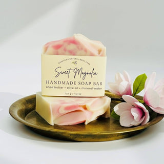Handmade soap bar with 'Sweet Magnolia' label on a gold plate with pink flowers.