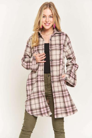 A woman modeling a long-sleeve plaid button-up shirt jacket in a dusty pink, brown, and beige pattern, worn open over a black top and olive green pants, against a plain white studio background.