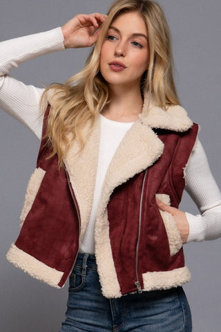 Woman wearing a burgundy vest with white fur lining against a gray background