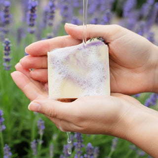 Hand holding a soap bar with lavender flowers in the background