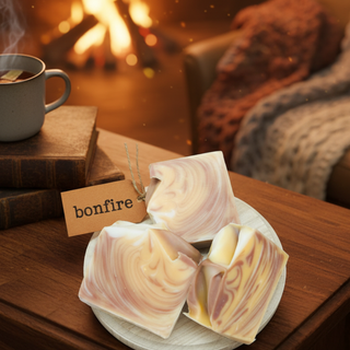 Marble-patterned soap bars on a wooden surface with a 'bonfire' tag, mug, and books in the background.