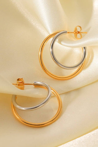 Pair of gold and silver hoop earrings on a beige fabric background