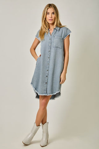 Woman wearing a light blue denim dress with white boots on a plain background