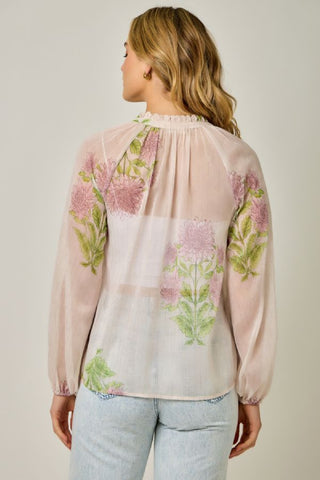 Woman wearing a sheer blouse with floral embroidery on a plain background