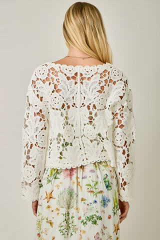 Woman wearing a white lace top over a floral dress on a plain background