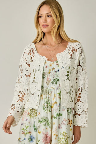 Woman wearing a floral dress with a white lace cardigan against a plain background