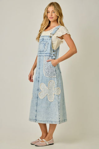 Woman wearing a denim dress with floral embroidery on a plain background