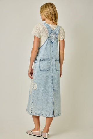 Woman wearing a light blue denim pinafore dress on a plain background