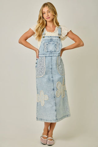 Woman wearing a denim dress with floral embroidery on a plain background