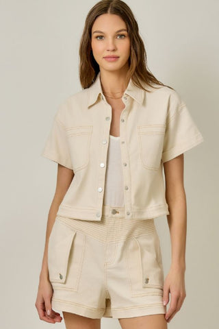 Woman wearing a beige outfit with a matching jacket and shorts on a plain background